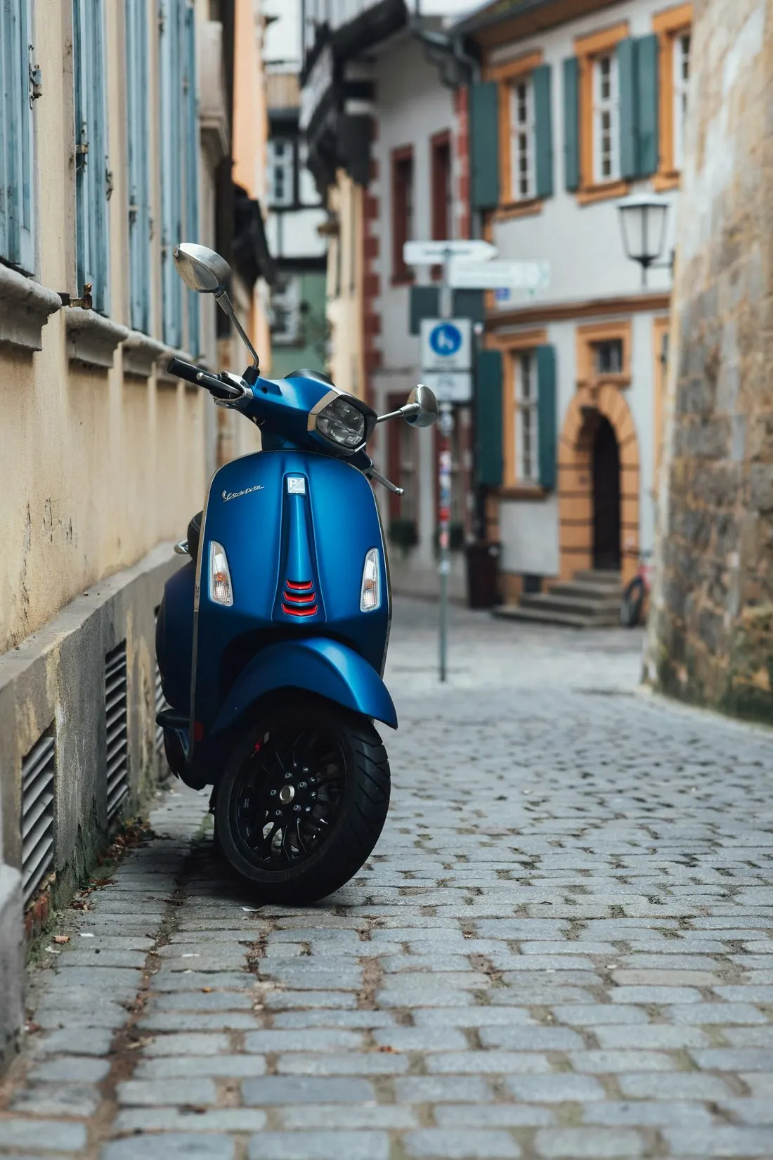 Blue Vespa 150 parked on a cobblestone street between historic buildings