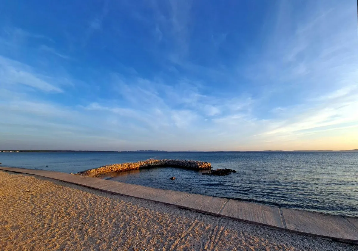 A quiet sandy beach at Privlaka at dusk, with a stone breakwater curving into calm water